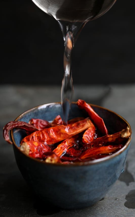 Hot water pouring over ceramic bowl with dried chilies in order to rehydrate them