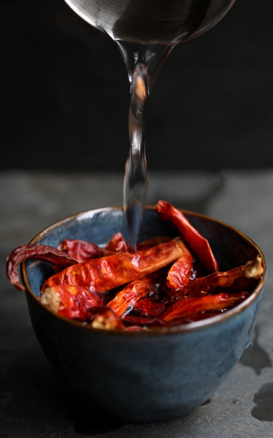 Hot water pouring over ceramic bowl with dried chilies in order to rehydrate them Hot water pouring over ceramic bowl with dried chilies in order to rehydrate them