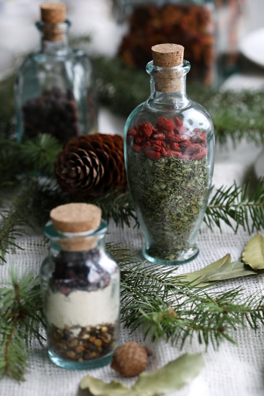 Decorative bottles filled with colorful herbs displayed with holiday foliage. 