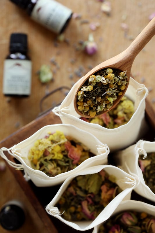 Filling herbal dream pillows with calming organic herbs and dried flowers. Helichrysum, rose buds, chamomile, and hops flowers in cotton bags for restful sleep. 