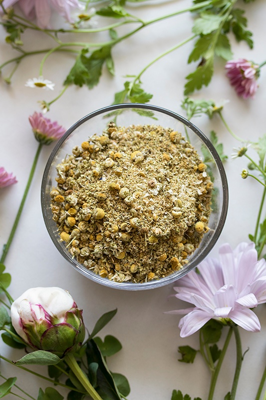 glass bowl with dried herb and dried flowers for a facial steam sitting on counter with fresh blooms