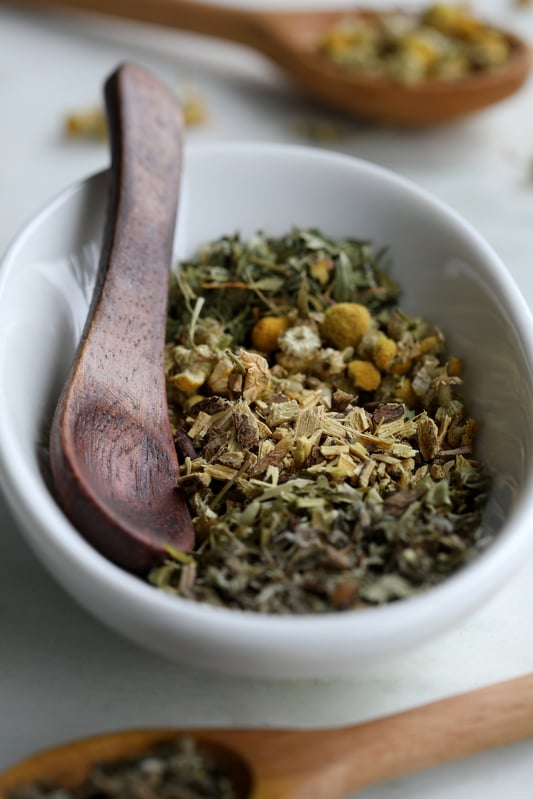 White bowl filled with a mixture of herbs and a rustic wooden spoon