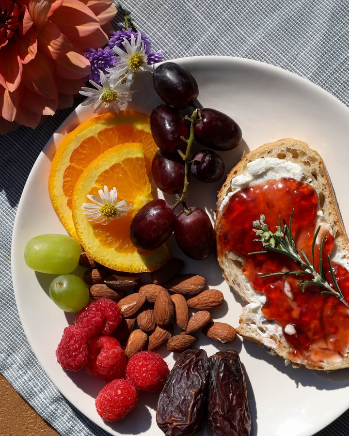 Hibiscus hot pepper jelly with cream cheese on baguette surrounded by fruit and nuts .