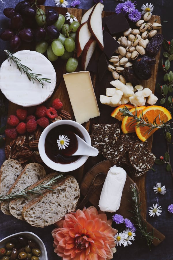 Cheese board with fruit, nuts, baguette, crackers, cheeses and hibiscus hot pepper jelly.