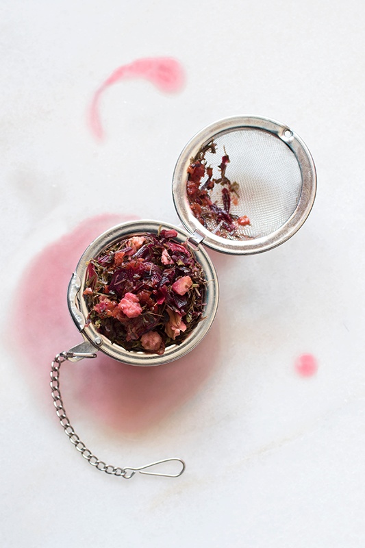 loose-leaf herbal tea made from hibiscus flowers and other herbs in a open strainer on a white counter