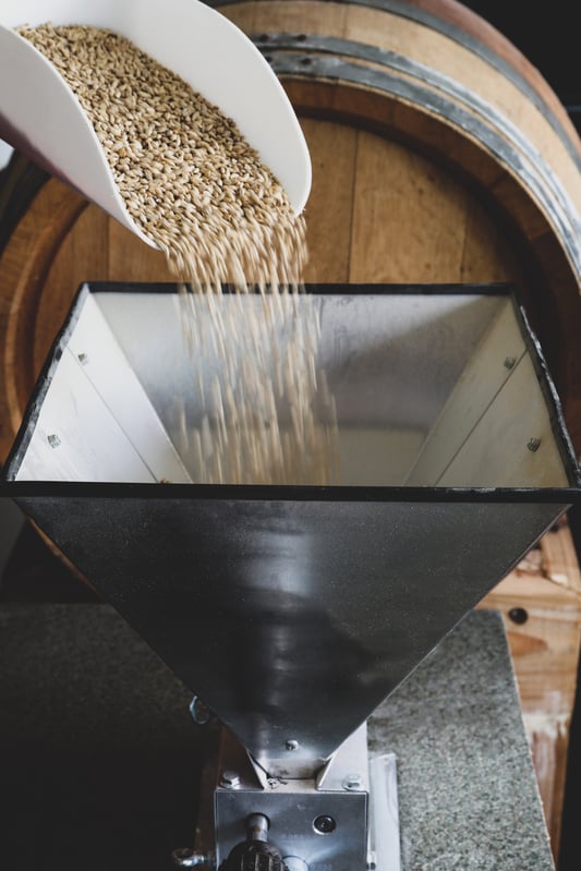 Scoop pouring grain into a a small grain mill for herbal beer making