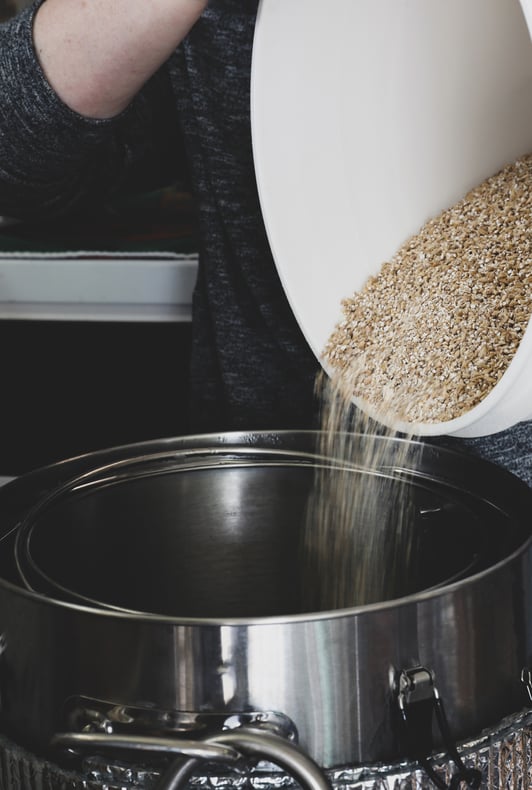 Pouring milled grain into pots with hot water for making herbal beer