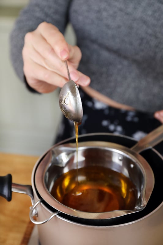 Spoon dropping honey into a double boiler in a pot