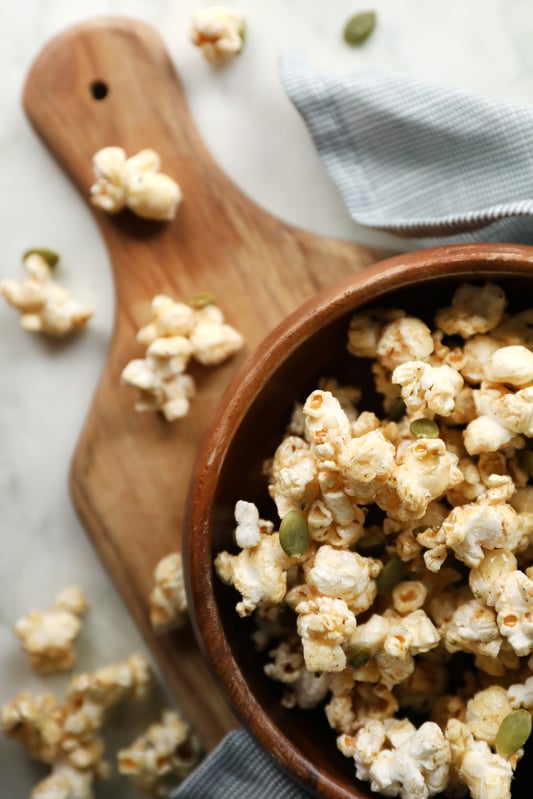A bowl of homemade caramel corn with pumpkin seeds, hemp seeds, and pumpkin pie spice. Perfect for fall snacking, sweet and spicy with chipotle powder.