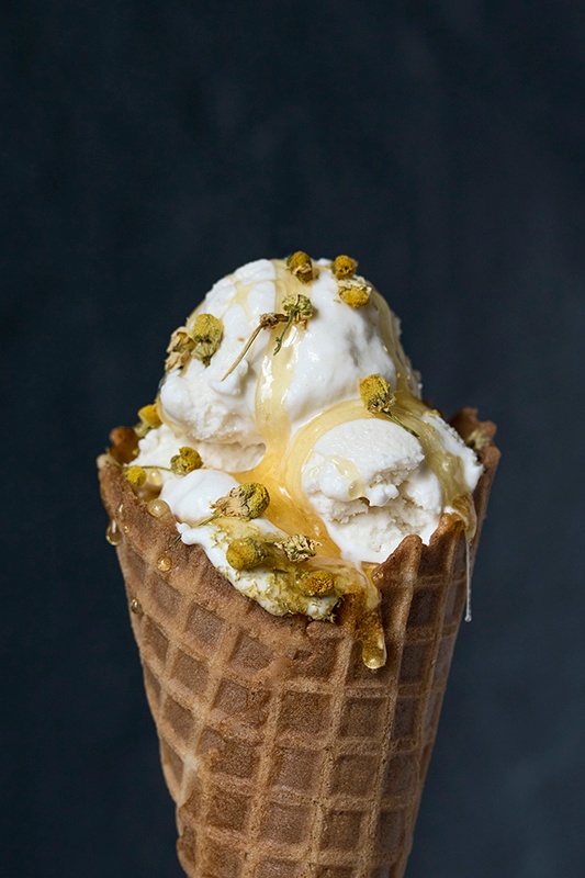 Ice cream cone filled with scoops of ice cream drizzled with honey and chamomile flowers