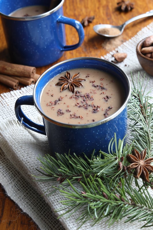 Camping mug with herbal hot chocolate sprinkled with herba and star anise, mug sitting on woven table cloth