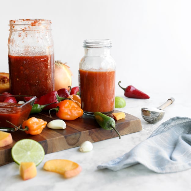 Jars of hot sauce surrounded by fresh colorful peppers, garlic, and lime slices. 