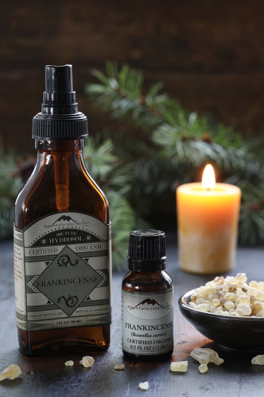 frankincense hydrosol and frankincense essential oil next to a bowl of frankincense resin with a candle in the background