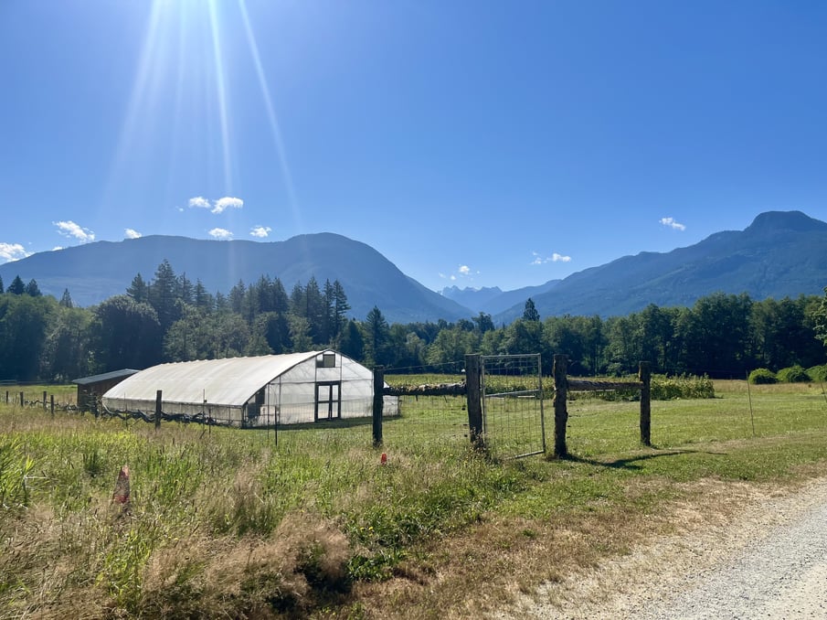 Green house set on a farm with hills in background. 