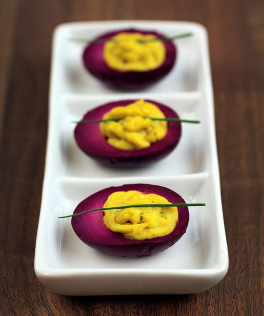 Magenta pickled curry deviled eggs on a white plate on wooden table