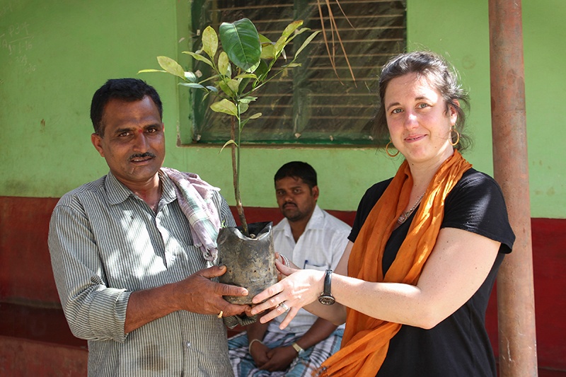 Indian farmer and COO from Mountain Rose Herbs holding sapling in front of a green building.