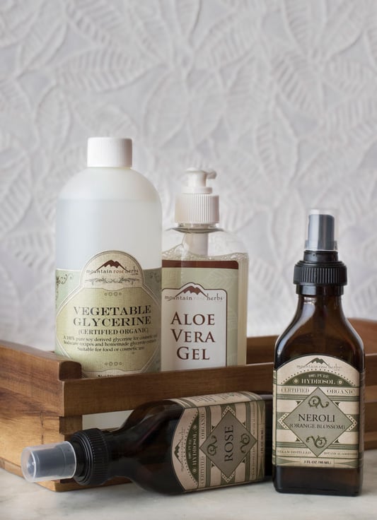 Ingredients for DIY body care including aloe vera gel and organic hydrosols on a tabletop