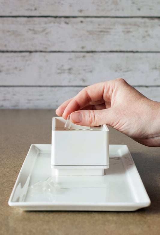 Hand placing empty capsule into white plastic capsule machine on porcelain plate base