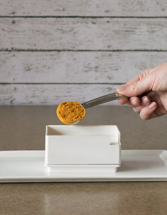 Hand measuring out 1 tablespoon of organic turmeric powder for placing into capsule machine