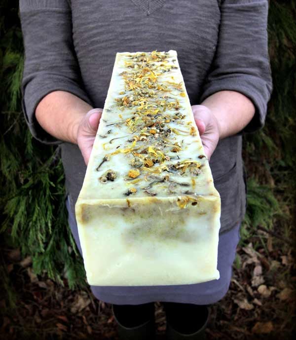 Person in gray dress holding block of finished soap with calendula and chamomile petals on top