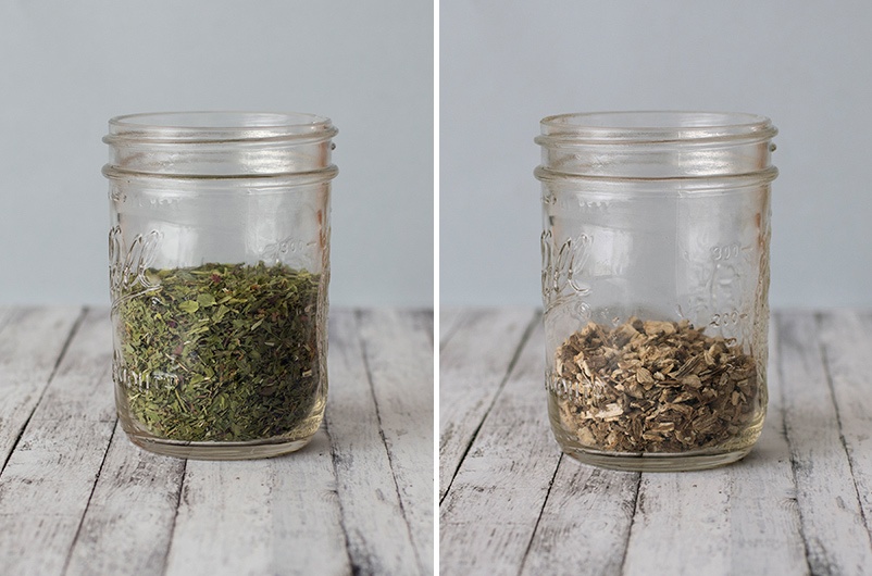 Dried herbs and roots in mason jars on light wooden table with blank background.