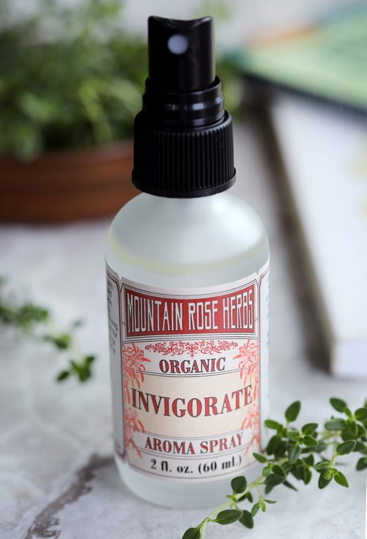 Frost glass bottle of Invigorate Aroma Spray with fresh herbal sprigs. 