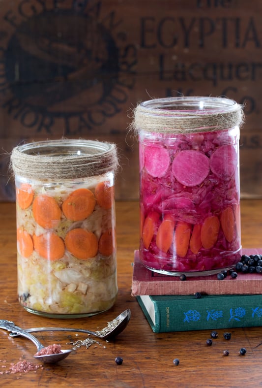 Jars of colorful homemade sauerkraut with ingredients around them