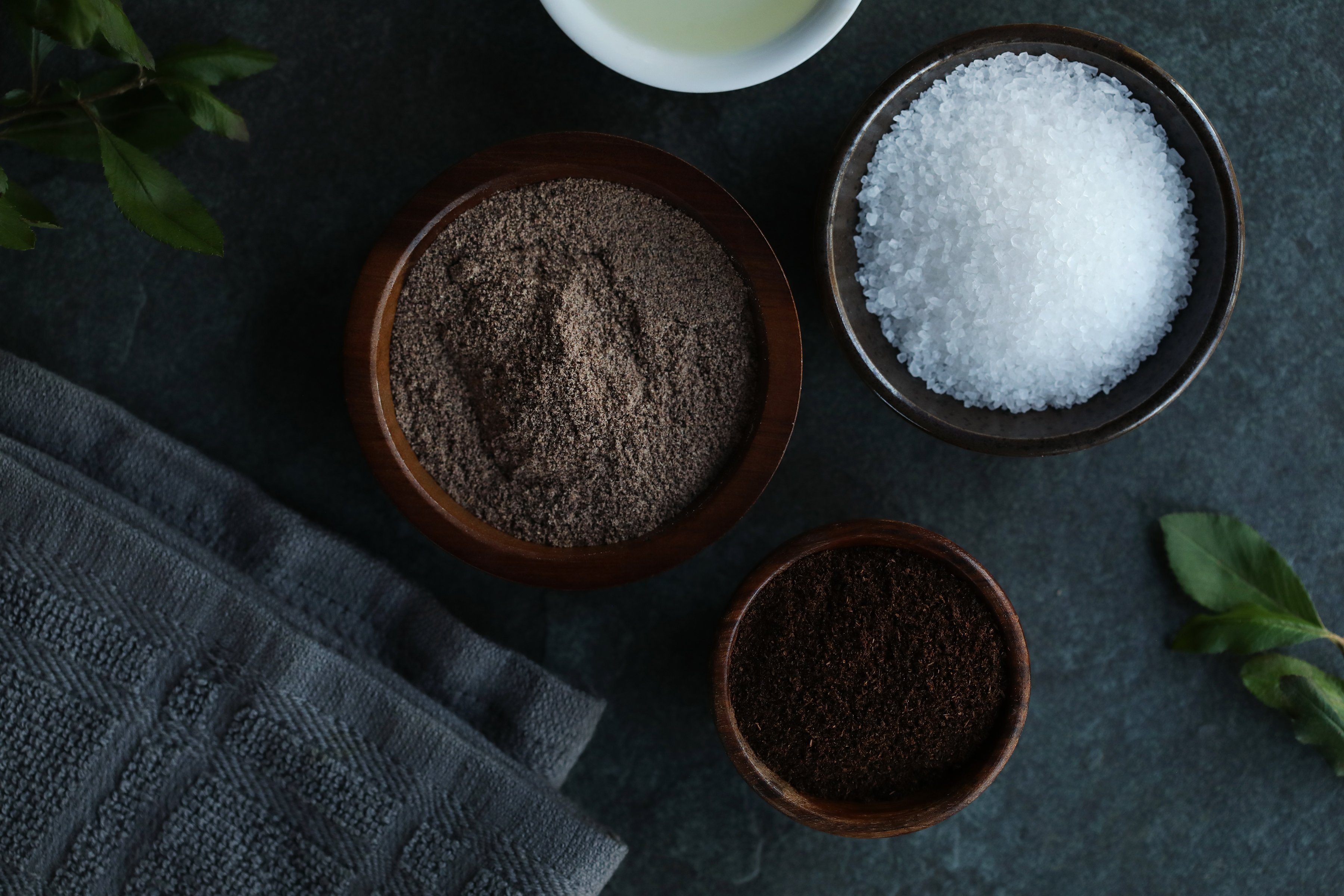 Ingredients are laid out for making a DIY body scrub. Ingredients include organic sweet almond oil, coarse sea salt, organic jojoba meal, and organic vanilla bean powder. 