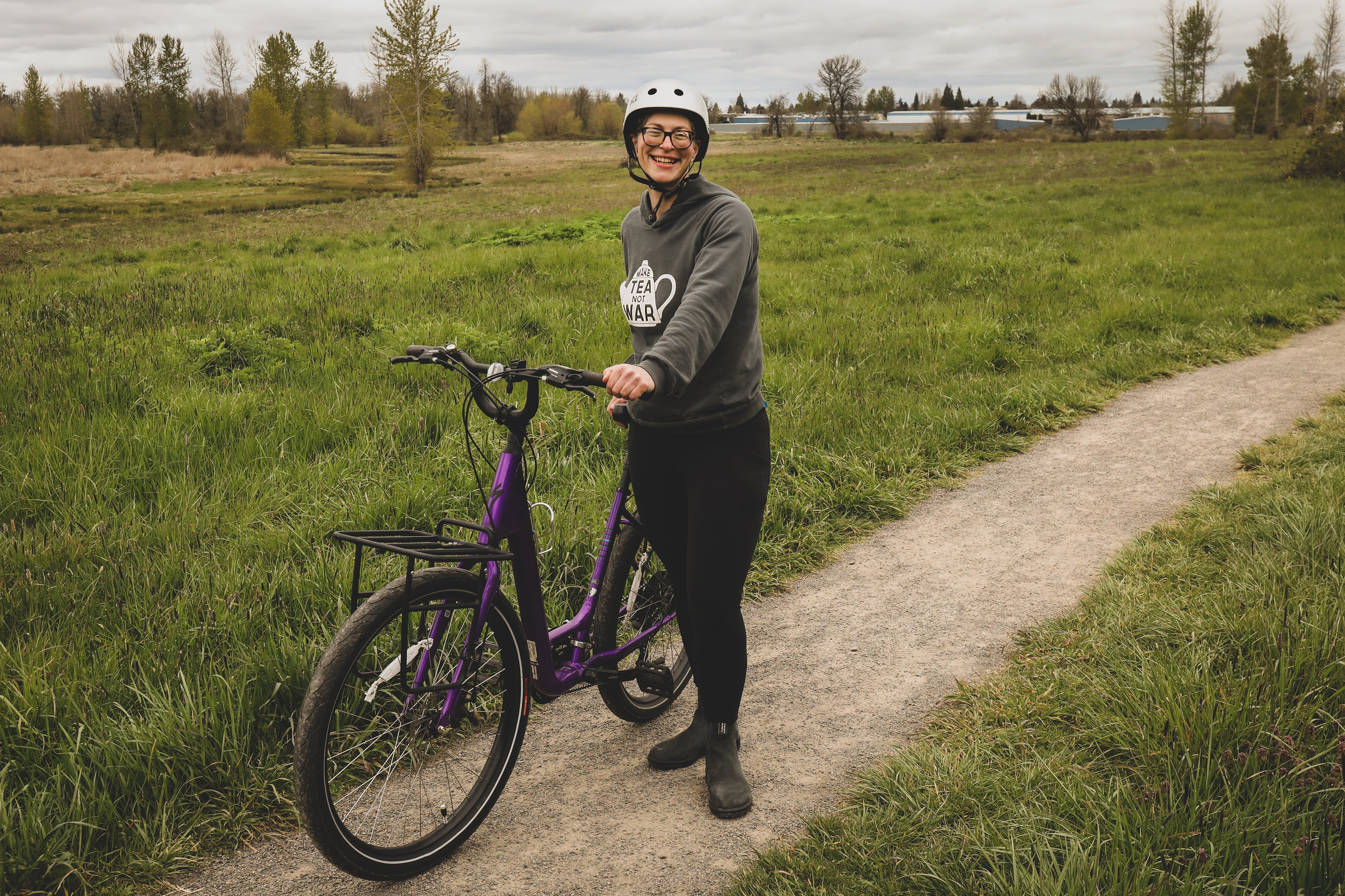 Woman standing in a field with a purple bike. 