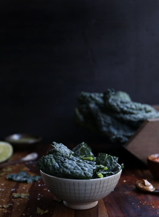 A white ceramic bowl filled to the brim with fresh organic Italian kale on a wooden cutting board.