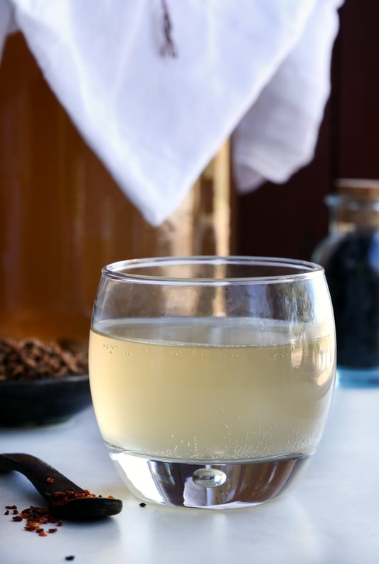 Small class of fizzy kombucha drink with botanicals in backround