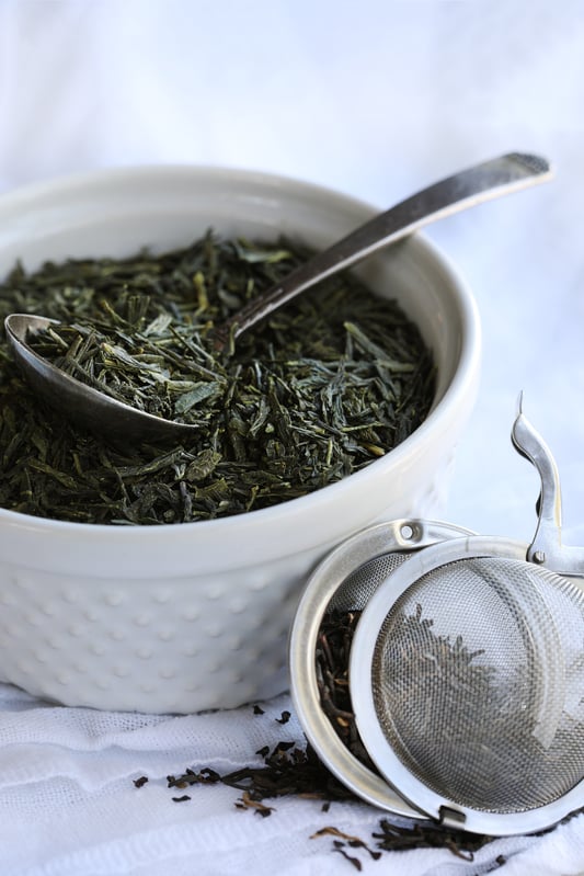 Fresh looking green tea in white [porcelain bowl with spoon and tea infuser filled with tea