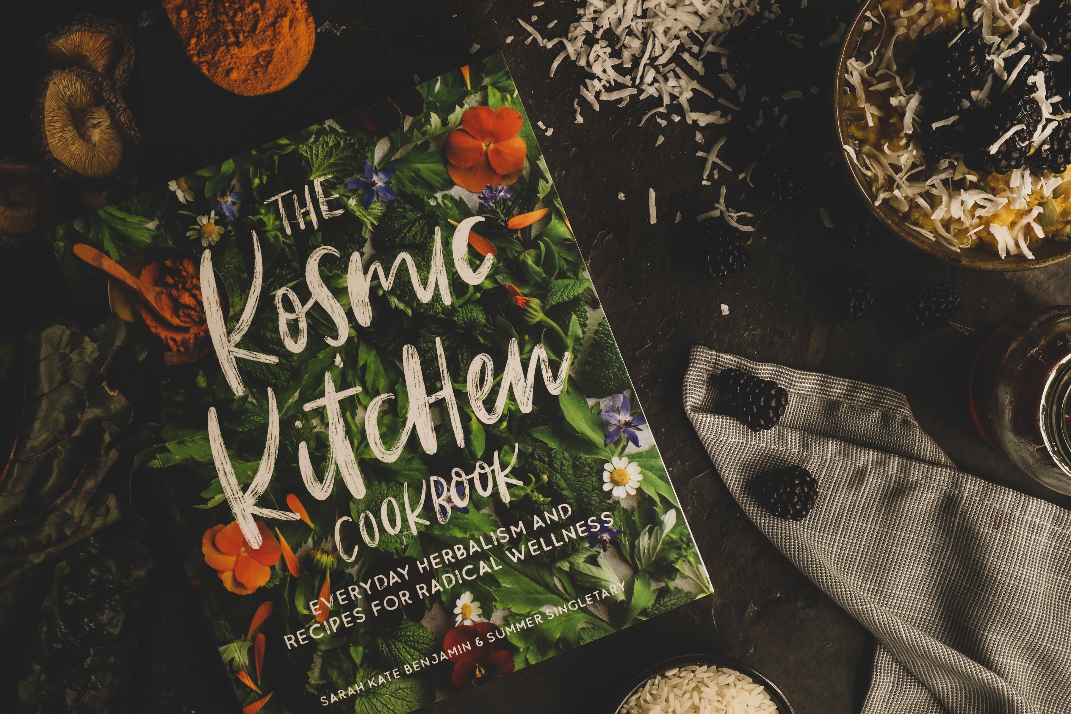 Kosmic Kitchen book surrounded by colorful ingredients. 