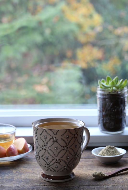 Ceramic mug filled with kava kava tea made from a french press sitting on window sill