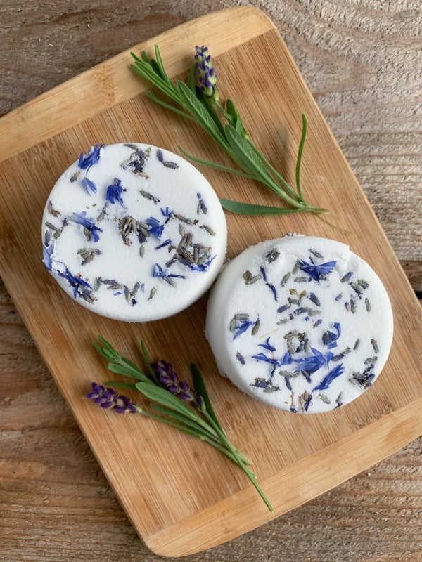 Two handmade bath bombs mixed with dried lavender flowers on a wooden cutting board surrounded by fresh sprigs of lavender