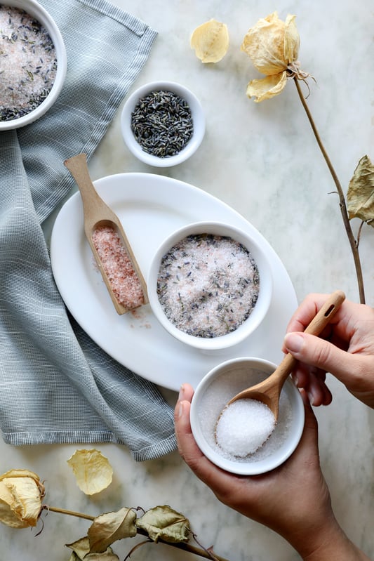 Lavender bath salts are prepared by combining epsom salt, sea salt, Himalayan pink salt, baking soda, and essential oils. The final solution is used to elevate the bathing experience with fragrance and skin smoothing qualities. 