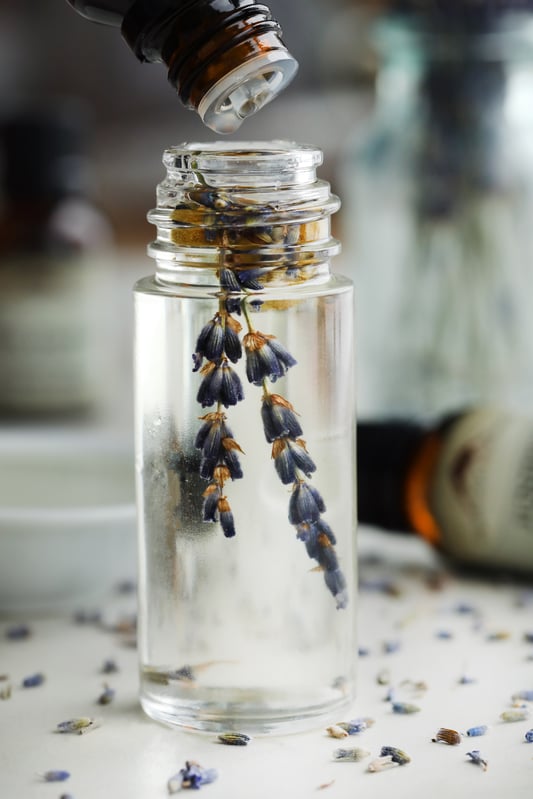 Clear bottle with lavender flowers and bottle of essential oil dropping into it.