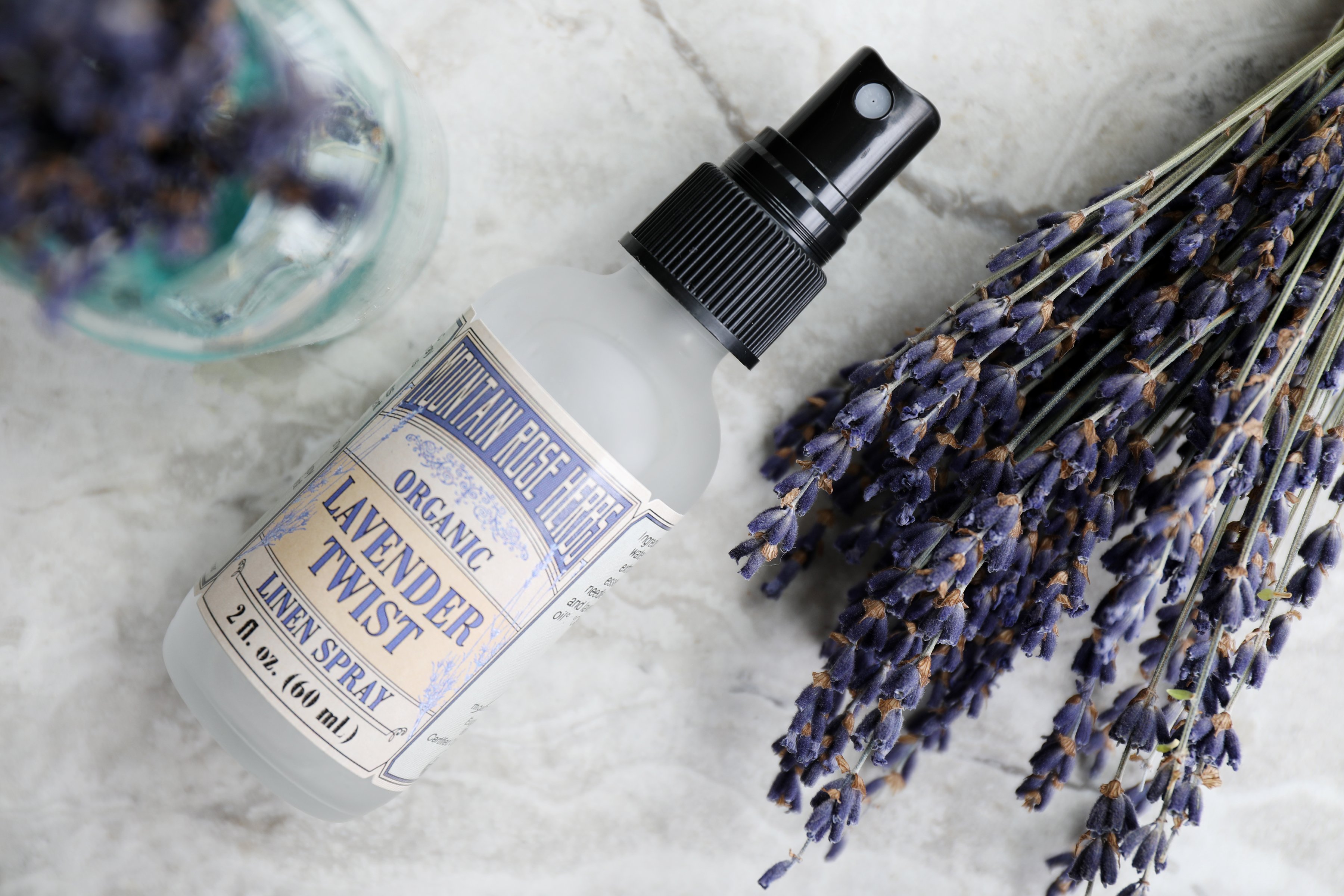 Bottle of Lavender Twist Aroma Spray with fresh sprigs of Lavender flowers. 