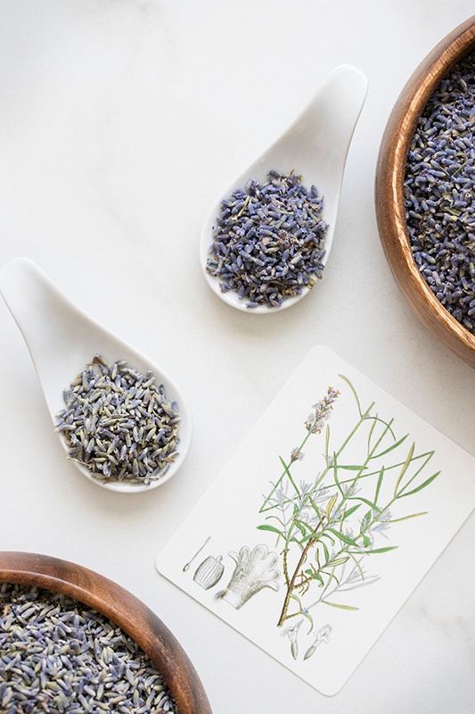 Spoonfulls of lavandin and lavender flowers on counter with herb card and bowl 