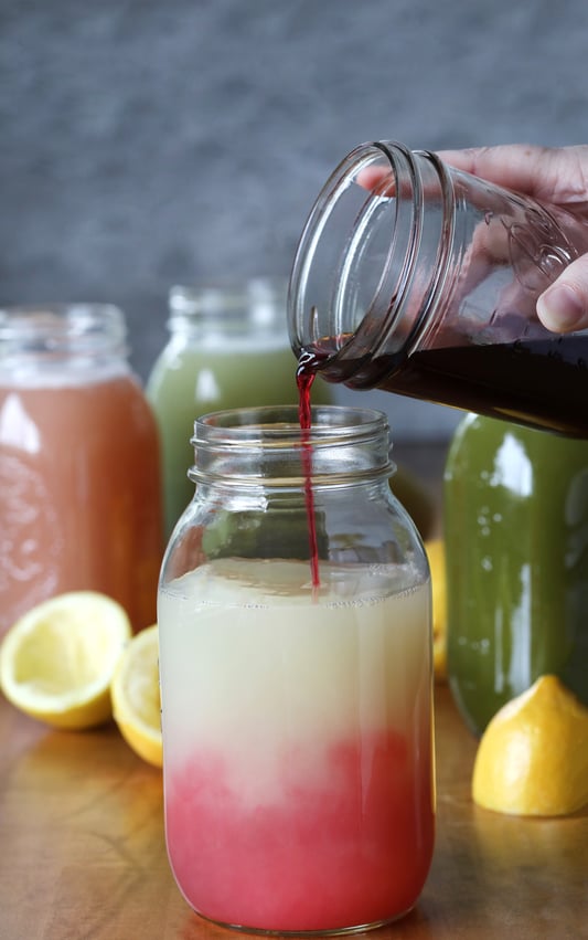 Hand pouring rich red fluid into mason jar of iced lemonade