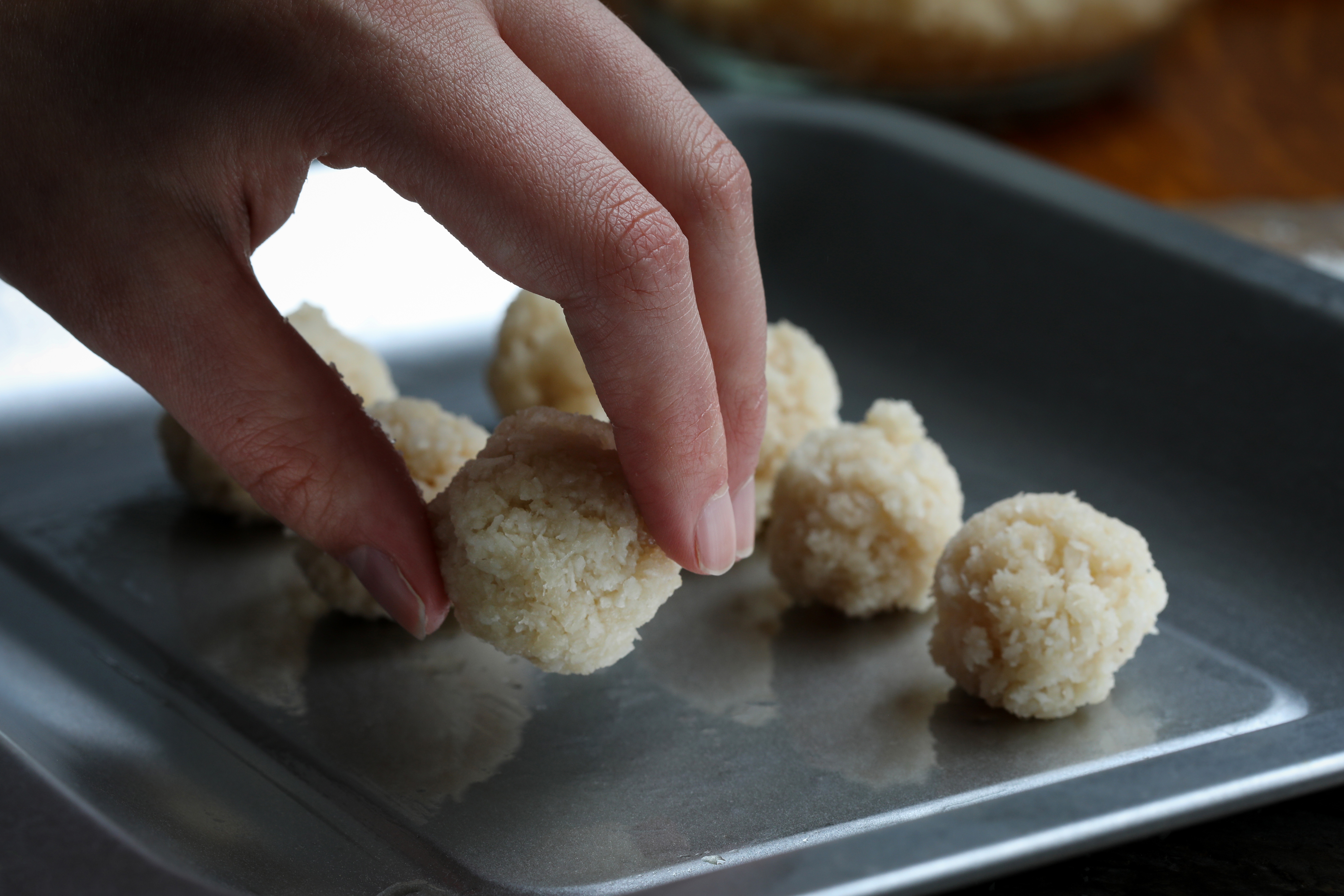 Hand placing coconut macaroon cookie balls on metal baking sheet