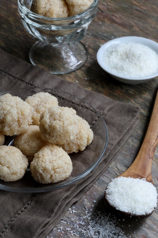 Organic coconut macaroon cookie balls on wood table with spoonful of coconut flakes