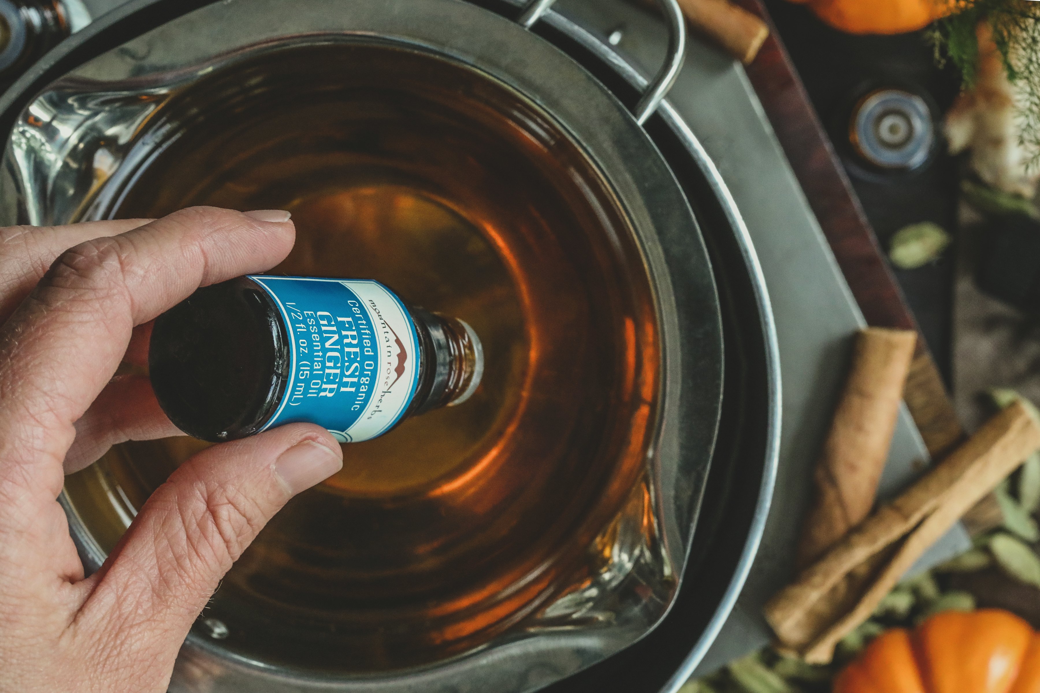 Fresh ginger essential oil being poured into a double boiler to make candle wax. 