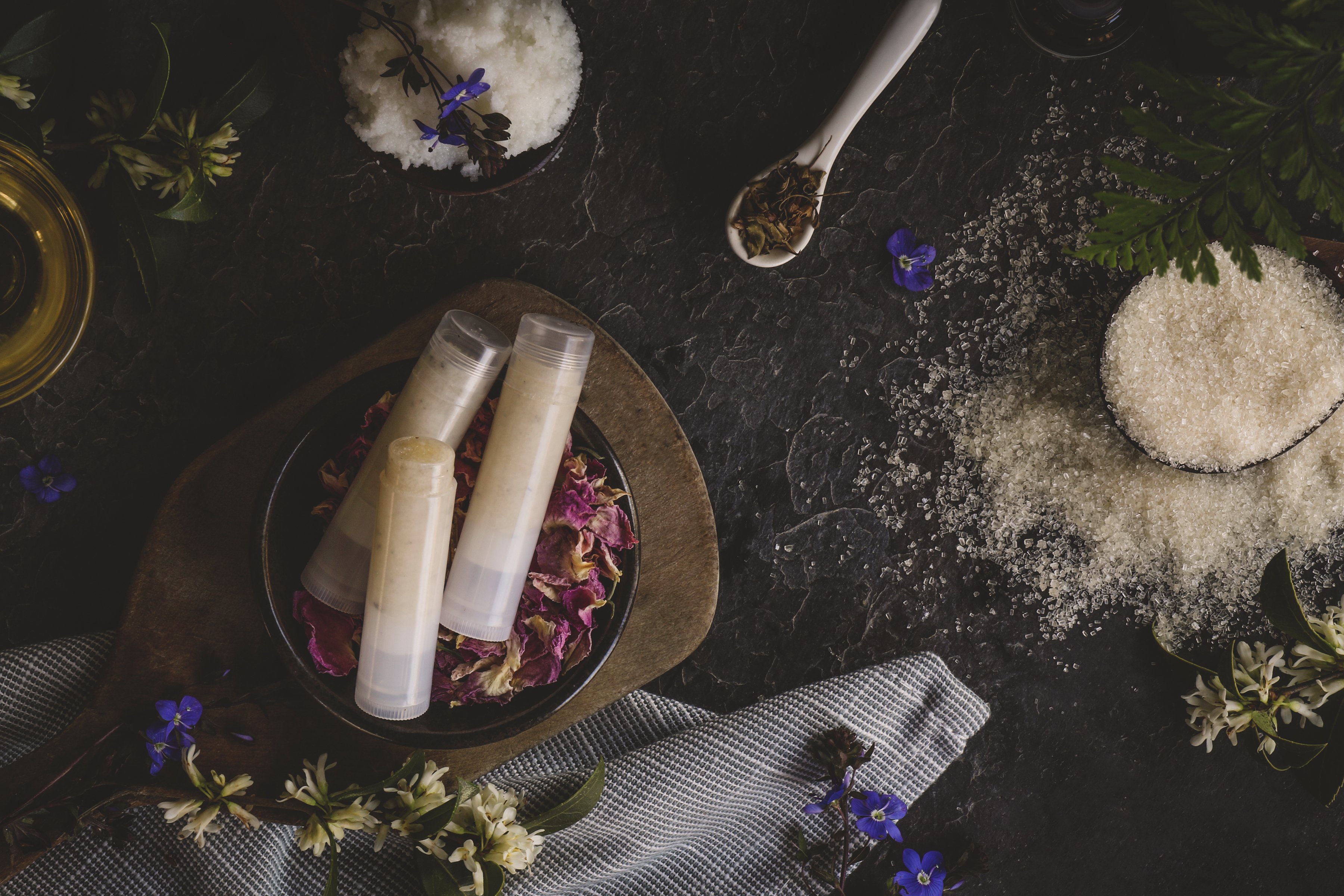 Display of lip balm tubes, salts, DIY ingredients and small purple flowers. 