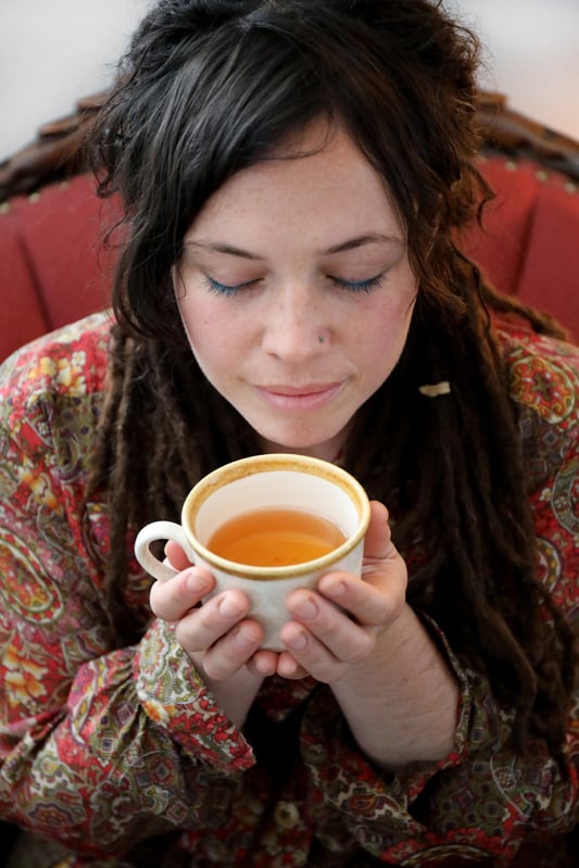 Young woman in paisley print dress holding cup of tea close to face to smell aroma