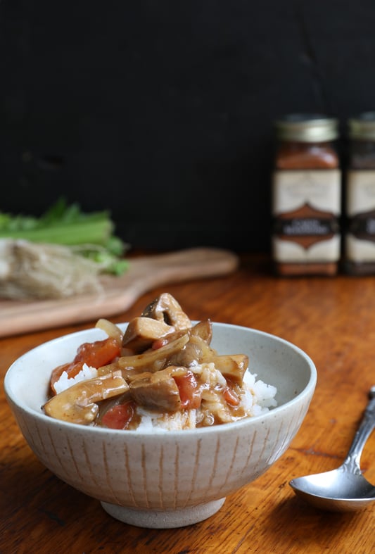 Vegetarian gumbo in bowl on top of rice sitting on wood countertop near cutting board