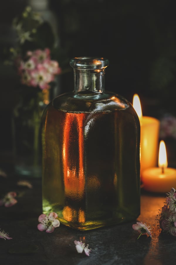 Square glass jar with massage oil- moody candles lit in the background. 