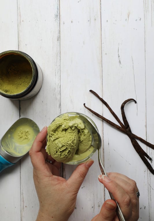 Hand holding crystal glass bowl filled with matcha ice cream with one hand with spoon and vanilla beans