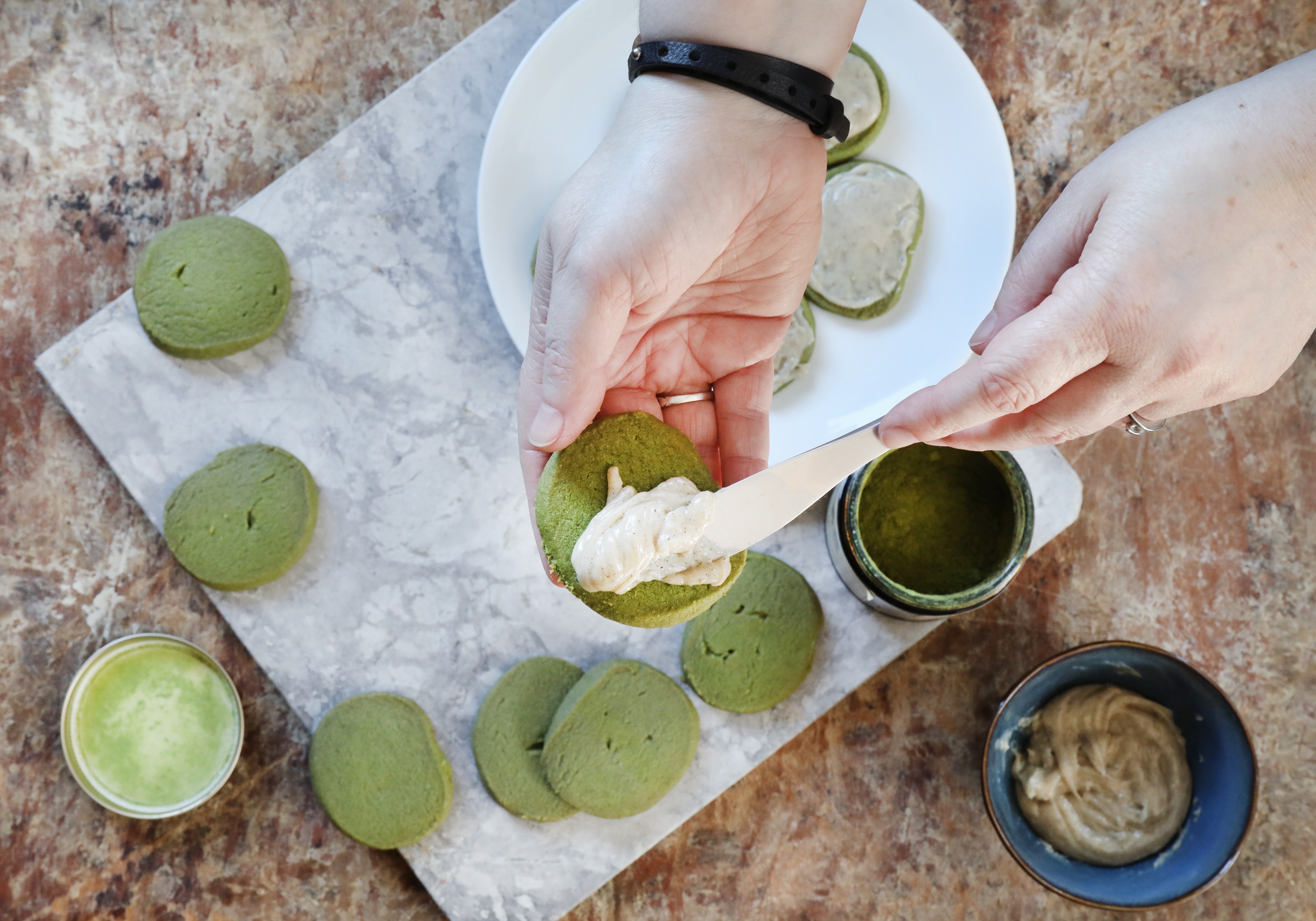 Hand with butter knife spreading vanilla bean glaze on shortbread matcha cookies