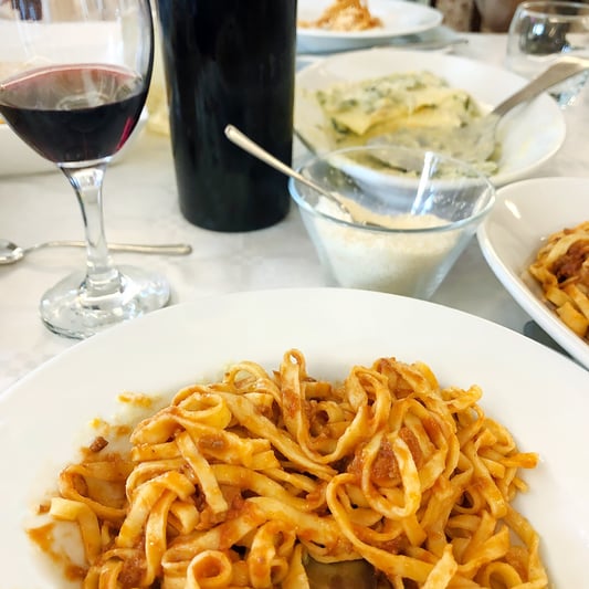 Table set with homemade Italian style meal, pasta with red sauce, glass of red wine, parmesean cheese.